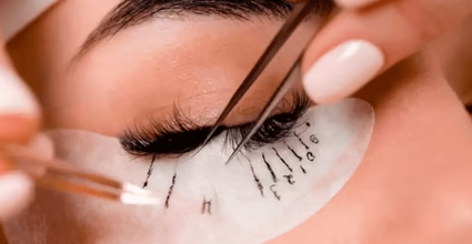 A close-up of an eye during eyelash extension application, with tweezers and protective eye patch.