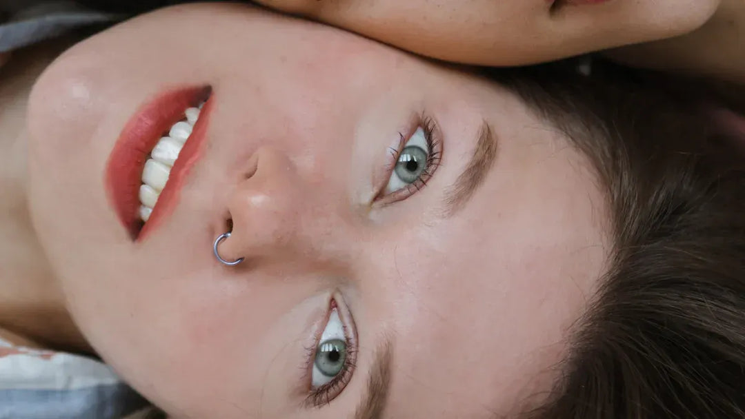 A close-up of a smiling woman with a nose ring and green eyes.