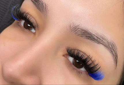 A person has long, thick eyelashes with blue tips, complemented by well-groomed eyebrows.