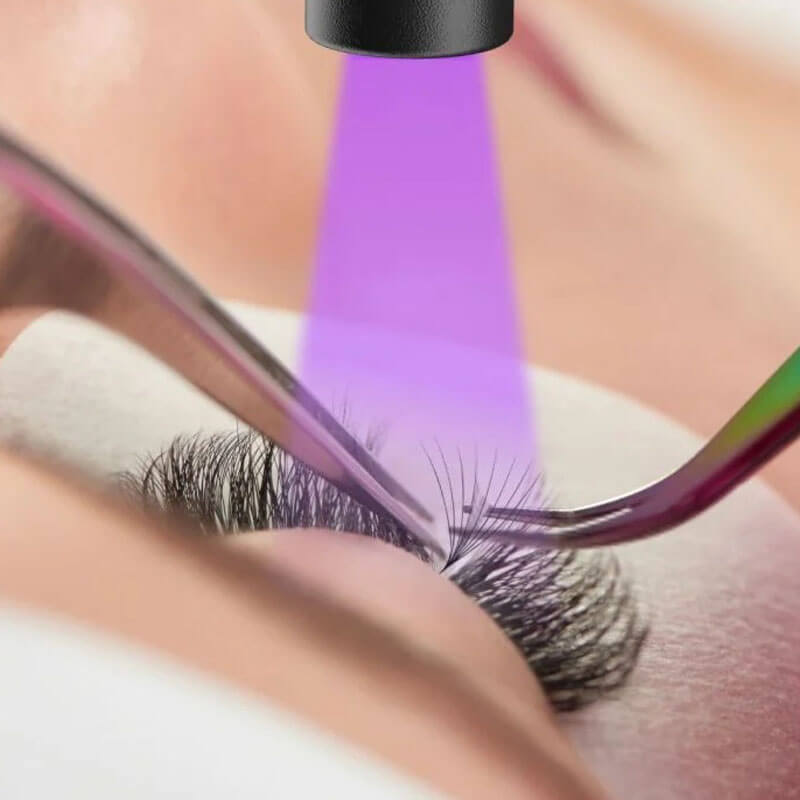 A close-up of an eyelash extension procedure with a purple UV light curing the adhesive.